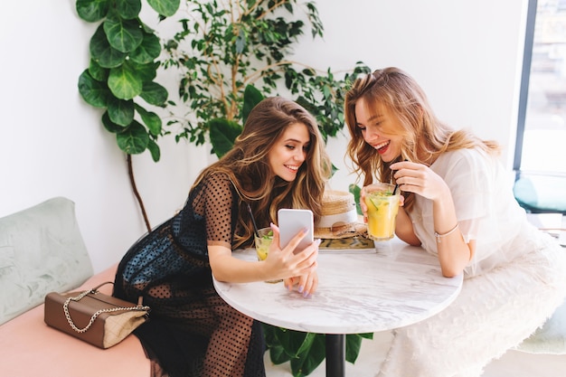 Dos chicas de pelo largo descansando en la cafetería con un interior moderno y riendo