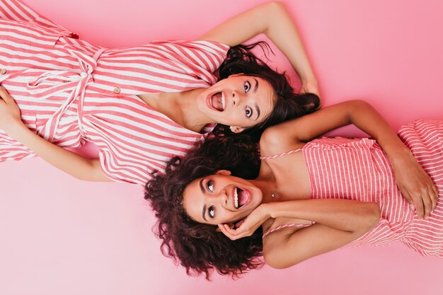 dos chicas de piel oscura con un cabello hermoso y rostros sorprendidos posan boca arriba.