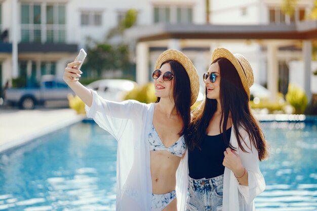 dos chicas relajándose junto a la piscina y tomando fotos en su teléfono