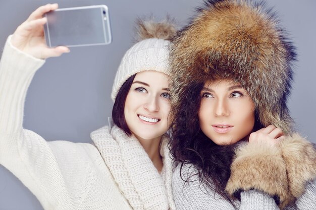 Dos chicas con ropa de invierno tomando fotos de selfie en un smartphone.