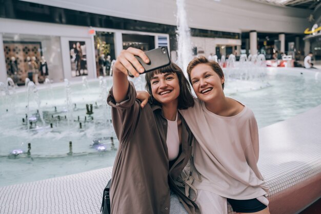 Dos chicas se toman una selfie en el centro comercial, al lado de una fuente