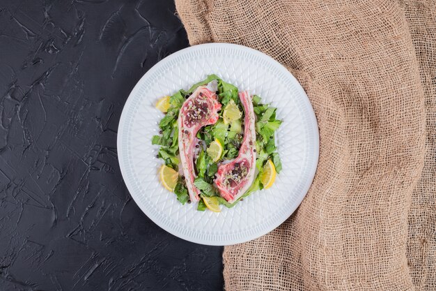 Dos chuletas de carne cruda en un plato blanco con rodajas de limón y verde.