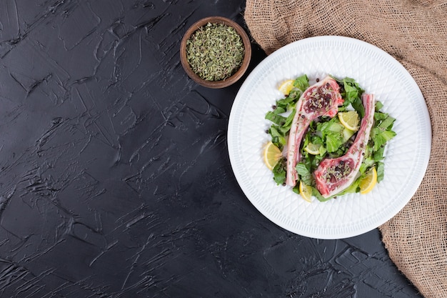 Dos chuletas de carne cruda en un plato blanco con rodajas de limón y verde.