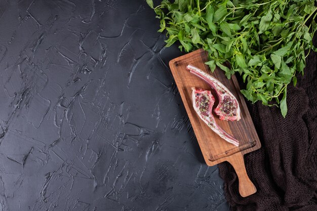 Dos chuletas de ternera cruda sobre tabla de madera con menta fresca.