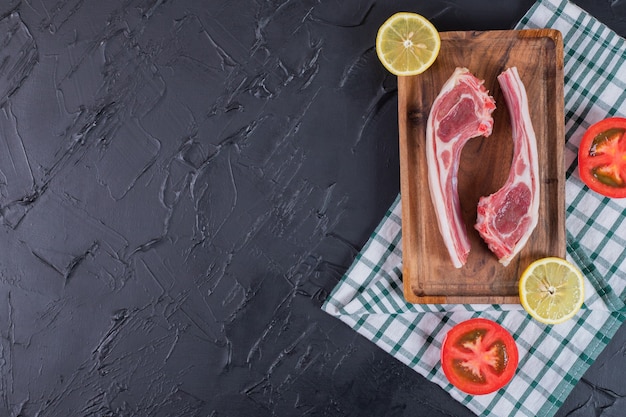 Foto gratuita dos chuletas de ternera cruda sobre tabla de madera con rodajas de limón y tomate.