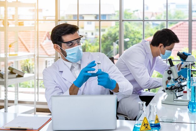 Dos científicos investigadores asiáticos y árabes que trabajan en laboratorios que realizan estudios de sustancias de riesgo biológico con equipo científico y microscopio