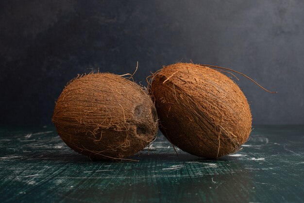 Dos cocos enteros sobre mesa de mármol.