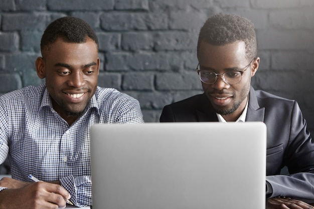 Dos colegas africanos felices usando laptop