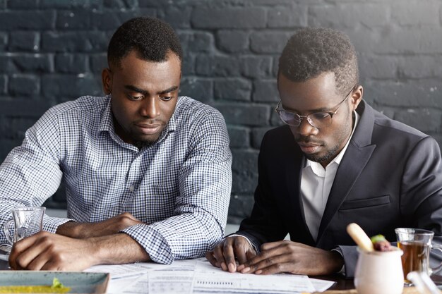 Dos colegas afroamericanos en ropa formal sentados en el escritorio con papeles mientras trabajan en el informe financiero