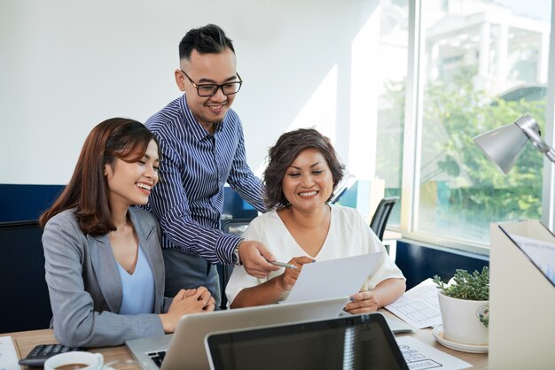 Dos colegas asiáticos femeninos y uno masculino discutiendo documentos juntos en la oficina