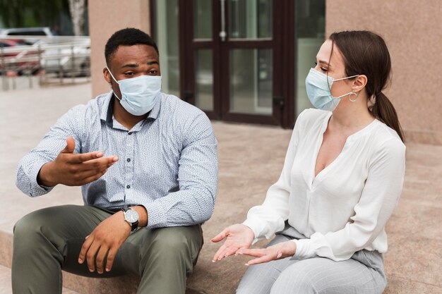 Dos colegas charlando al aire libre durante la pandemia con máscaras