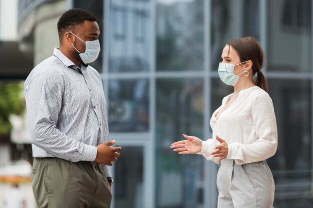 Dos colegas charlando al aire libre durante la pandemia con máscaras