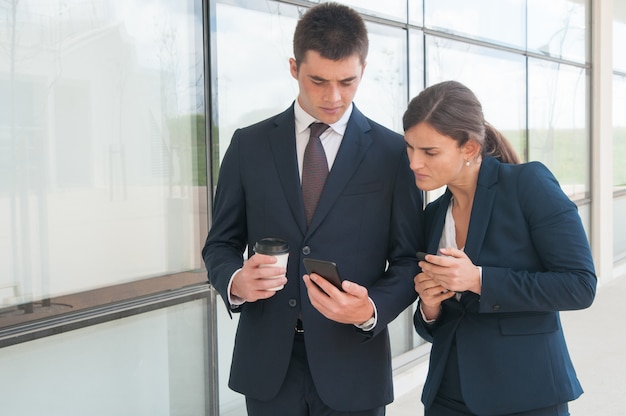 Dos colegas enfocados con teléfonos que comparten información.