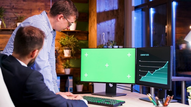 Dos colegas de oficina mirando una pantalla de computadora verde. Luz de luna y luz azul