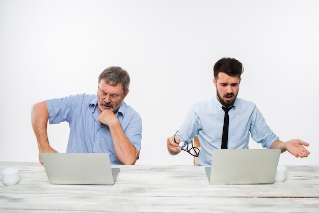 Foto gratuita los dos colegas que trabajan juntos en la oficina sobre fondo blanco. ambos miran las pantallas de las computadoras. concepto de emociones negativas y malas noticias.