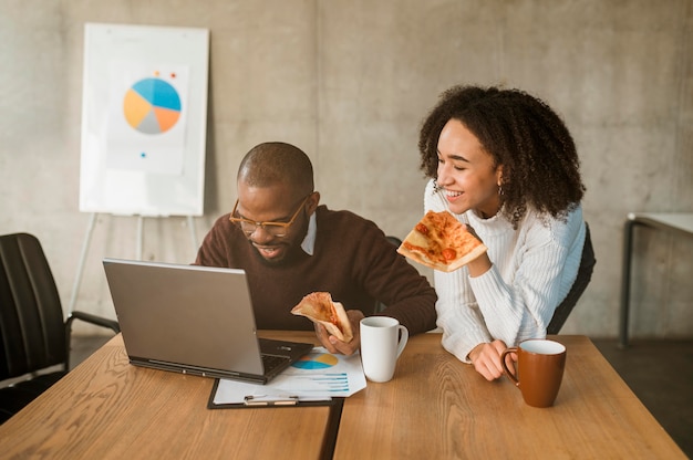 Dos colegas sonrientes con pizza durante un descanso de la reunión de oficina