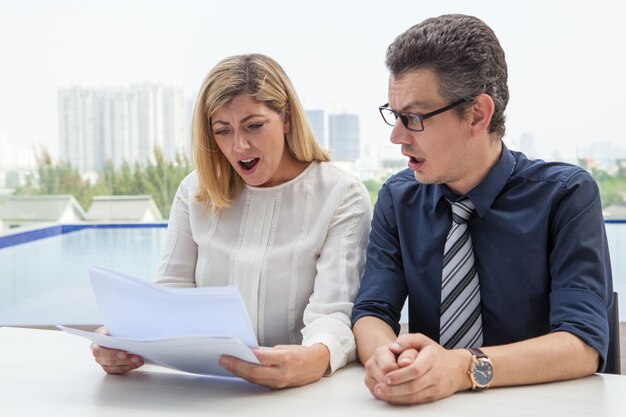 Dos colegas sorprendidos mirando a través del informe de negocios al aire libre.