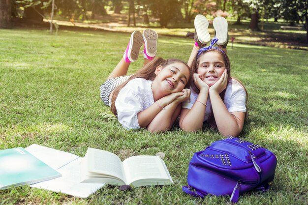 Dos colegialas tumbados en la hierba con las cabezas apoyadas en las manos sonriendo