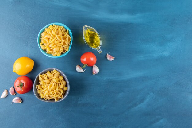 Dos coloridos tazones de pasta cruda con tomates rojos frescos y un limón entero.