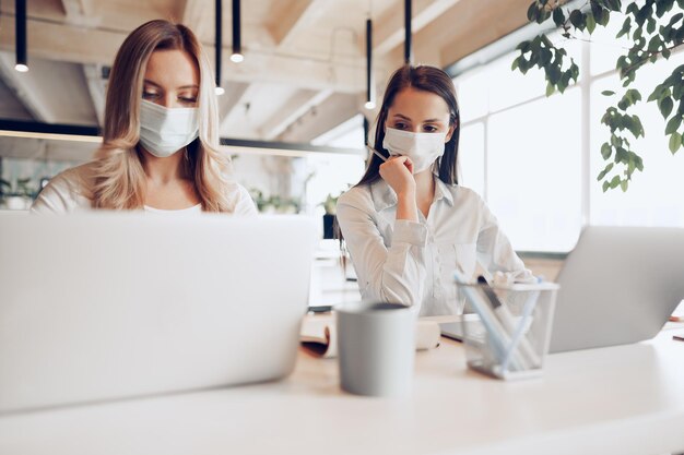 Dos compañeras que trabajan en la oficina junto con máscaras médicas