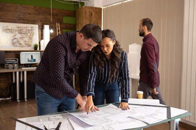 Dos compañeros arquitectos de pie a la mesa y discutiendo el proyecto. Oficina moderna