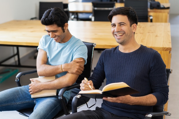 Dos compañeros estudiando, leyendo libros de texto y riendo