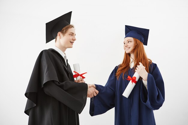 Dos compañeros graduados se dan la mano sonriendo con diplomas.