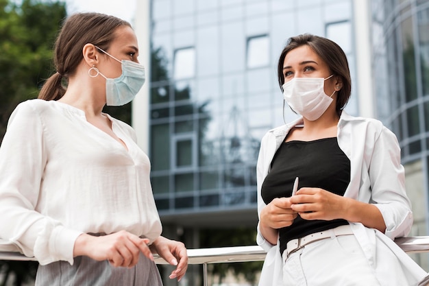 Dos compañeros de trabajo charlando al aire libre durante la pandemia mientras usan máscaras médicas