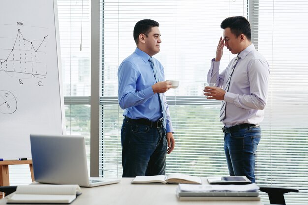 Dos compañeros de trabajo discutiendo la carga de trabajo en la taza de café