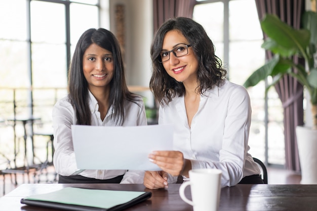 Dos compañeros de trabajo femeninos sonrientes que discuten el documento en café.
