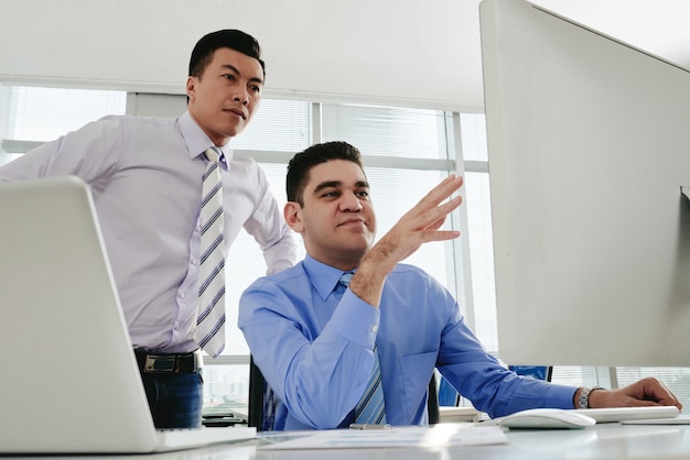 Dos compañeros de trabajo masculinos que colaboran en un proyecto en la computadora de la oficina