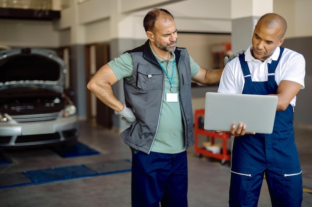 Dos compañeros de trabajo que usan una computadora portátil mientras trabajan en un taller de reparación de automóviles