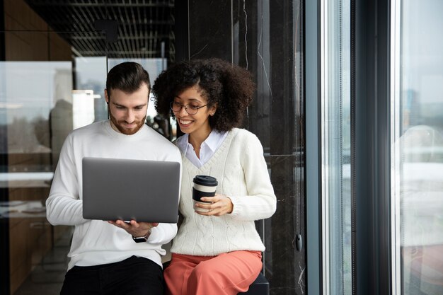 Dos compañeros de trabajo que usan una computadora portátil para trabajar y toman café