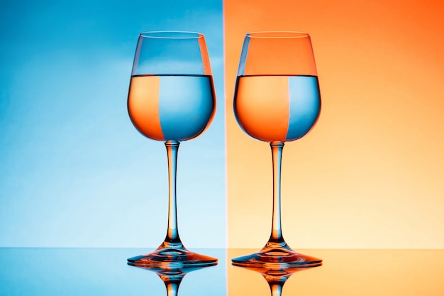 Dos copas con agua sobre fondo azul y naranja.