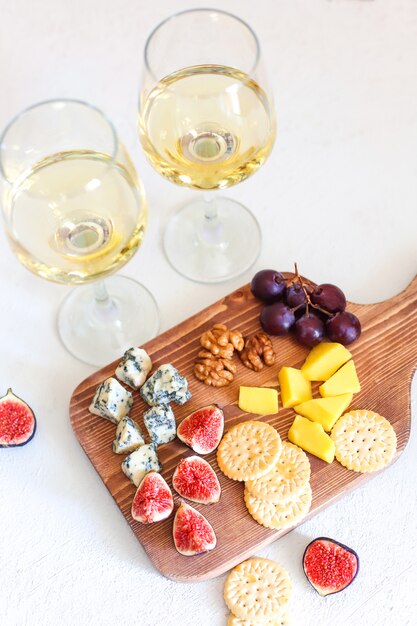 Dos copas de vino blanco y tabla de quesos con nueces