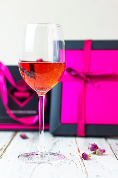 Foto gratuita dos copas de vino rosado en la mesa de madera blanca con cajas de regalo rosa