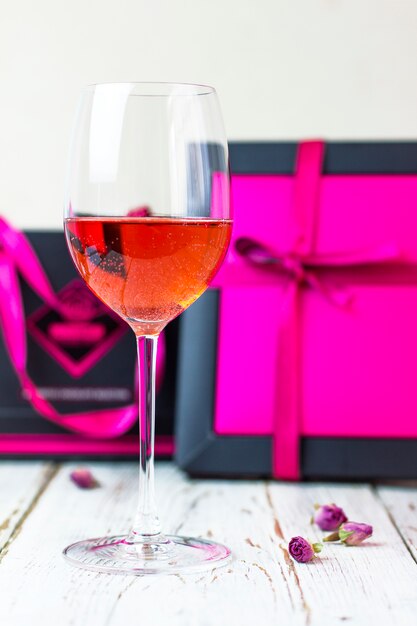 Dos copas de vino rosado en la mesa de madera blanca con cajas de regalo rosa