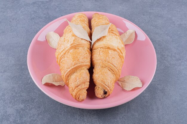 Dos croissant francés recién horneado en placa rosa.