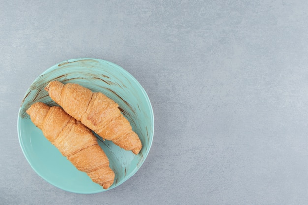 Foto gratuita dos croissants en el plato, sobre el fondo de mármol. foto de alta calidad