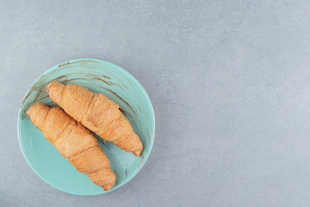 Dos croissants en el plato, sobre el fondo de mármol. Foto de alta calidad