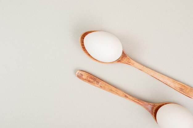 Dos cucharas de madera con huevos de gallina blanca.
