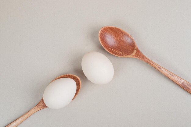 Dos cucharas de madera con huevos de gallina blanca.