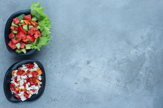 Dos cuencos de ensalada de pastor junto a un cuenco de ensalada de pimiento y coliflor sobre mármol.