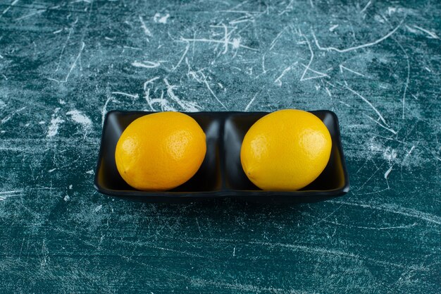 Dos cuencos de limones maduros con hojas, sobre el fondo de mármol. Foto de alta calidad