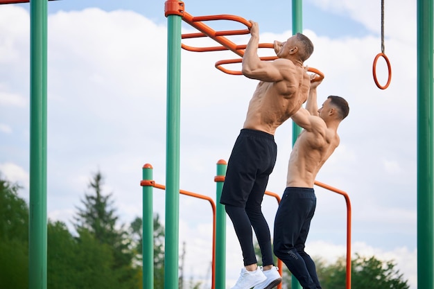 Dos culturistas haciendo ejercicios para brazos en campo deportivo