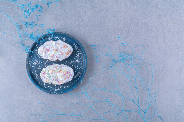 Dos cupcakes dulces frescos con chispas de colores y crema sobre una tabla de madera azul.