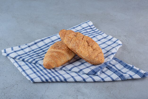 Dos deliciosos croissants dulces con mantel sobre piedra.