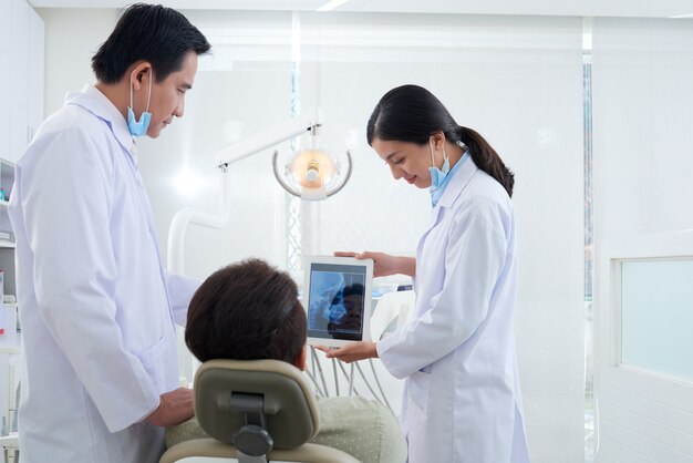 Dos dentistas asiáticos demostrando radiografía de la mandíbula del paciente en tableta