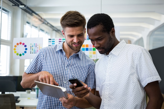 Dos diseñadores gráficos masculinos que usa la tableta digital y teléfono móvil