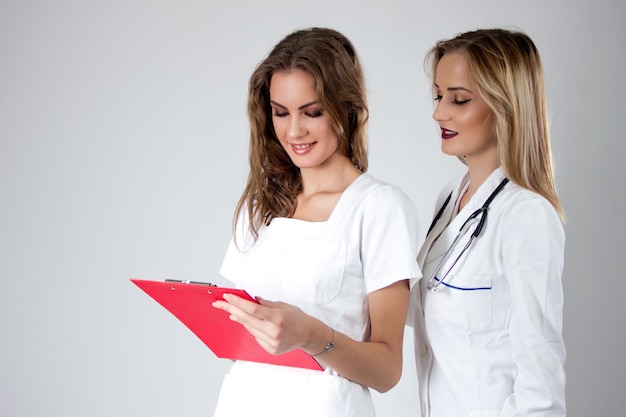 Dos doctores bastante jovenes de las mujeres, enfermeras que miran a través del expediente médico del paciente.